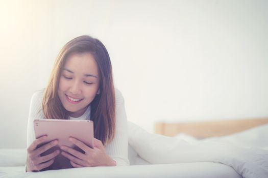 woman asian lying in bedroom with digital tablet touching with finger in morning sunlight