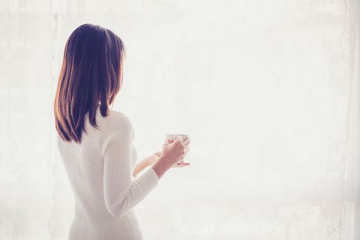 Beautiful young woman asian behind holding drinking coffee at a window.
