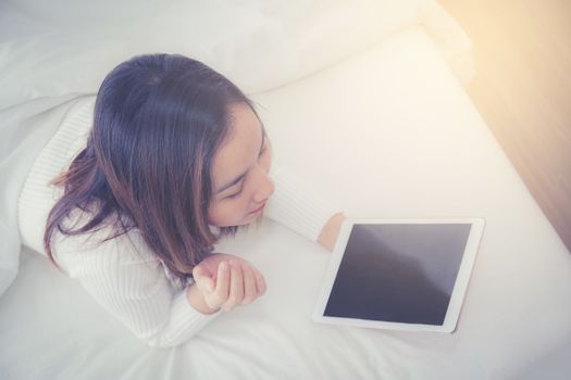 woman asian lying in bedroom with digital tablet touching with finger in morning sunlight