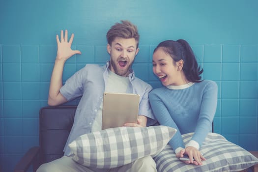Cute loving couple is using tablet in sofa - They are sitting and smiling and glad with success.