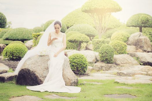 bride touch on phone in wedding dress on garden.