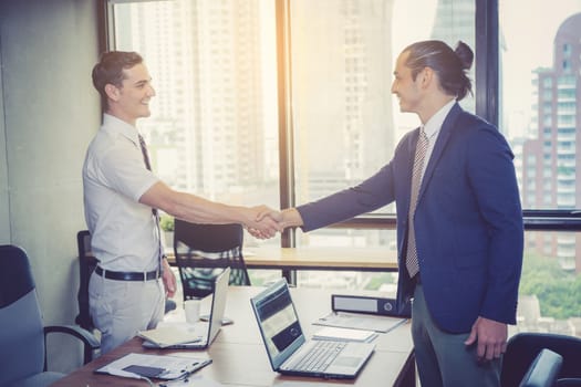 Two happy successful business partner shaking hands in the office.