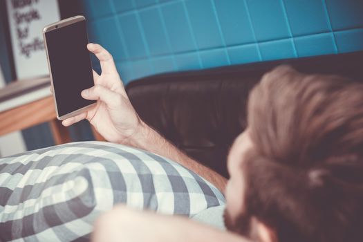 Happy man watching media content in a smart phone sitting on a couch at home, Top side view mock up background