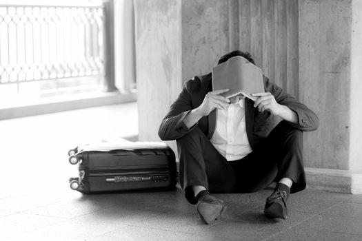 Stressed asian businessman bankrupt with sitting at outdoor and book close face black and white picture.