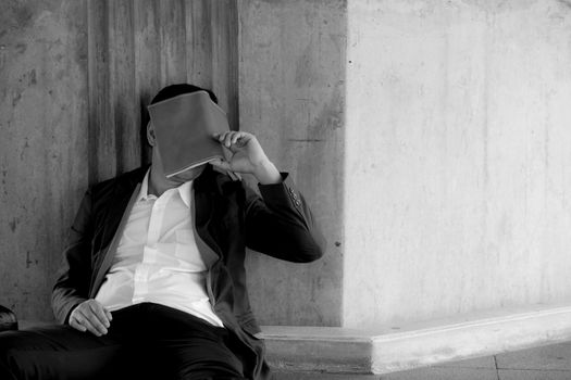 Stressed asian businessman bankrupt with sitting at outdoor and book close face black and white picture.