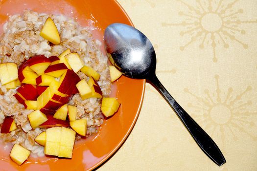 oatmeal porridge with chopped fresh peach in a plate with a spoon, vegetarian breakfast.