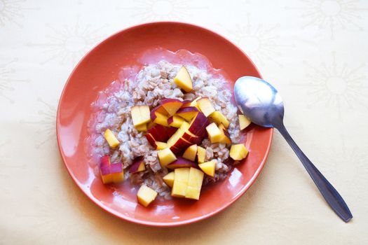 oatmeal porridge with chopped fresh peach in a plate with a spoon, vegetarian breakfast.