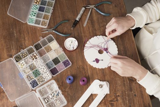 Lifestyle concept, work from home to reinvent your life: top view of woman hands making macrame knots the fuchsia thread creating an earring on kumihimo tools on wooden table