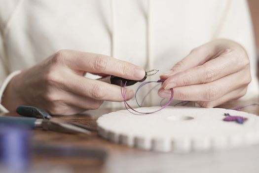 Lifestyle concept, work from home to reinvent your life: close-up of woman hands making macrame woman burns the wire with the appropriate tool to finish the job on kumihimo tools on wooden table