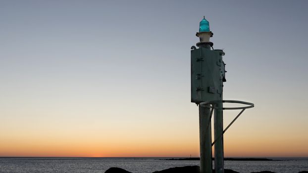 The sea at dawn or sunset with a small lighthouse in the harbor in the foreground