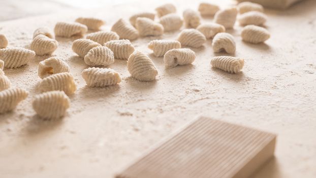 Close up of homemade vegan gnocchi pasta with wholemeal flour on the wooden chopping board with back light morning sunlight bokeh effect, traditional Italian pasta