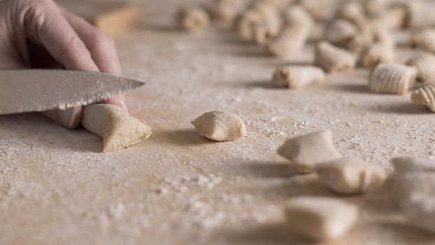 Close up process of homemade vegan gnocchi pasta with wholemeal flour making. The home cook cuts the dough on the wooden chopping board , traditional Italian pasta, woman cooks food in the kitchen