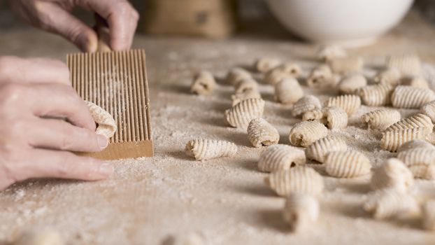 Close up process of homemade vegan gnocchi pasta with wholemeal flour making. The home cook crawls on the special wooden tool the gnocco , traditional Italian pasta, woman cooks food in the kitchen