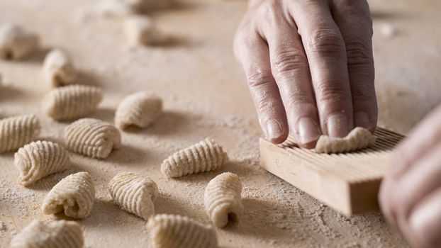 Close up process of homemade vegan gnocchi pasta with wholemeal flour making. The home cook crawls on the special wooden tool the gnocco , traditional Italian pasta, woman cooks food in the kitchen