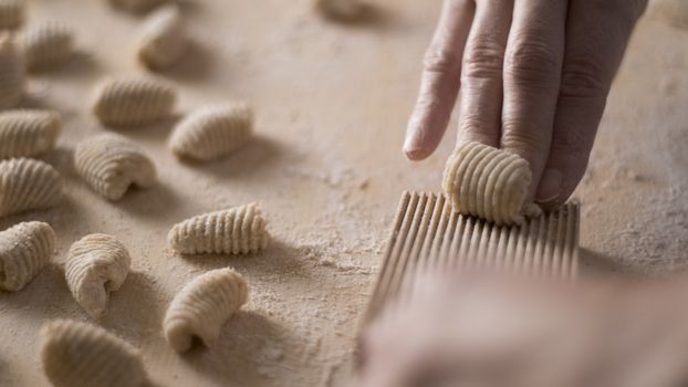 Close up process of homemade vegan gnocchi pasta with wholemeal flour making. The home cook crawls on the special wooden tool the gnocco , traditional Italian pasta, woman cooks food in the kitchen