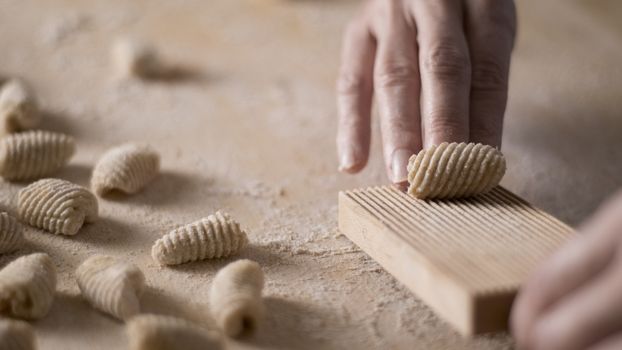 Close up process of homemade vegan gnocchi pasta with wholemeal flour making. The home cook crawls on the special wooden tool the gnocco , traditional Italian pasta, woman cooks food in the kitchen