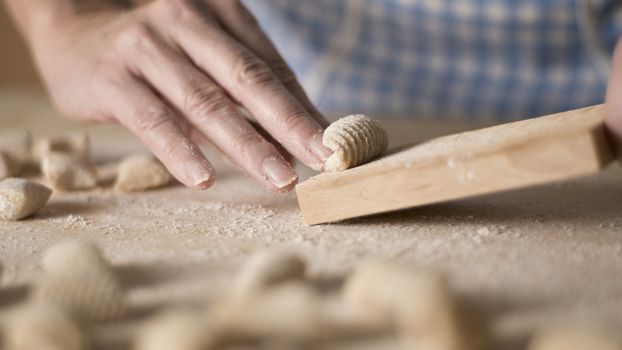 Close up process of homemade vegan gnocchi pasta with wholemeal flour making. The home cook crawls on the special wooden tool the gnocco , traditional Italian pasta, woman cooks food in the kitchen