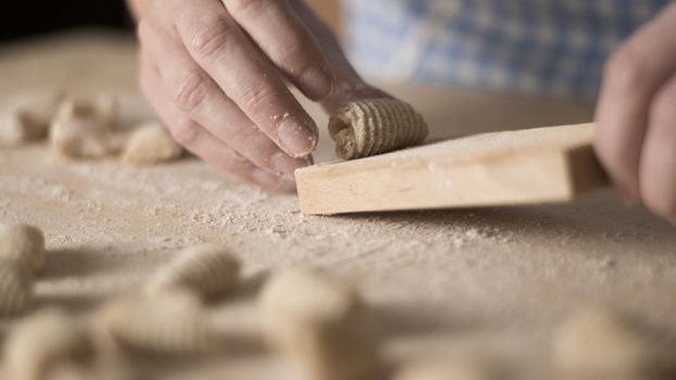 Close up process of homemade vegan gnocchi pasta with wholemeal flour making. The home cook crawls on the special wooden tool the gnocco , traditional Italian pasta, woman cooks food in the kitchen