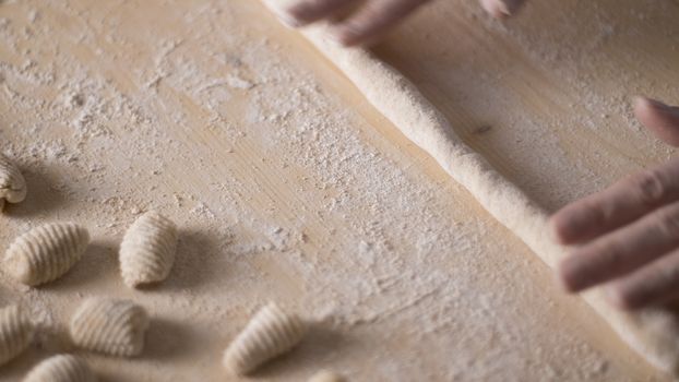 Close up process of homemade vegan gnocchi pasta with wholemeal flour making. The home cook rolls the dough on the wooden chopping board , traditional Italian pasta, woman cooks food in the kitchen