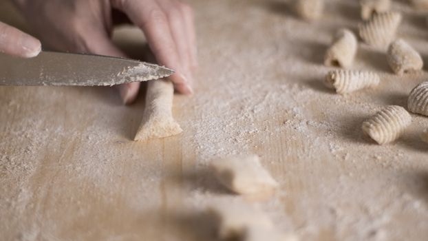 Close up process of homemade vegan gnocchi pasta with wholemeal flour making. The home cook cuts the dough on the wooden chopping board , traditional Italian pasta, woman cooks food in the kitchen