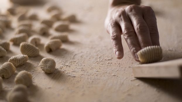 Close up process of homemade vegan gnocchi pasta with wholemeal flour making. The home cook crawls on the special wooden tool the gnocco , traditional Italian pasta, woman cooks food in the kitchen