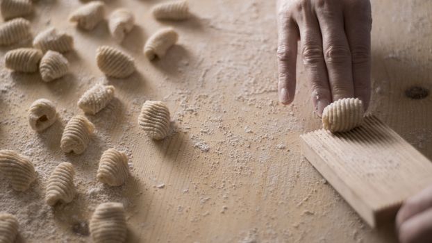 Close up process of homemade vegan gnocchi pasta with wholemeal flour making. The home cook crawls on the special wooden tool the gnocco , traditional Italian pasta, woman cooks food in the kitchen