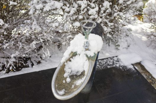 A snow covered drinking fountain in a public park. Cold water fountain with the background of snowy bushes on a cold day in Australia.