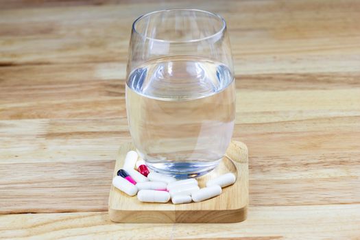 the white many capsules with Water in a glass on wood table 