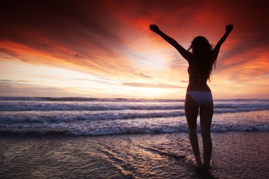 Woman in bikini walking with rised hands on the beach at sunset. Bali island, Indonesia