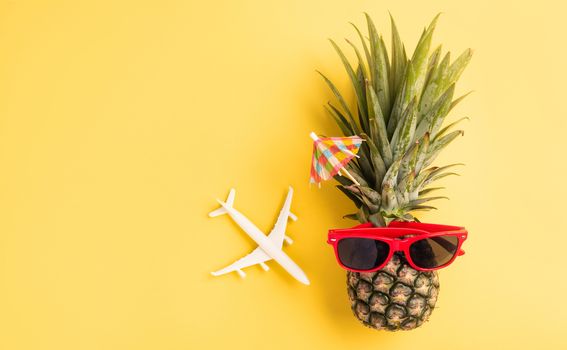 Celebrate Summer Pineapple Day Concept, Top view flat lay of funny fresh pineapple in sunglasses with model plane and starfish, in studio isolated on yellow background, Holiday summertime in tropical