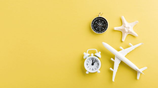 World Tourism Day, Top view flat lay of minimal toy model plane, airplane, starfish, alarm clock and compass, studio shot isolated on a yellow background, accessory flight holiday concept