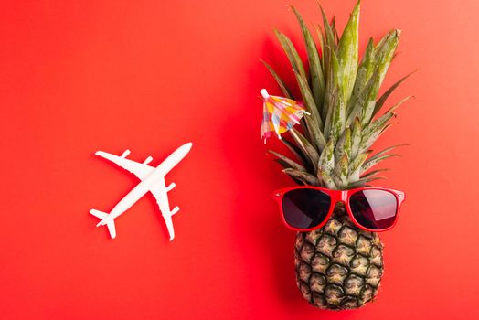 Celebrate Summer Pineapple Day Concept, Top view flat lay of funny fresh pineapple wear red sunglasses with model plane, isolated on red background, Holiday summertime in tropical