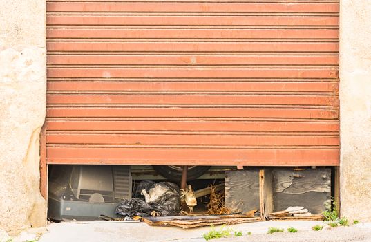View of half-open old rolling gate garage with garbage