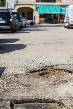 Close-up of pot hole on asphalt road with parking cars

