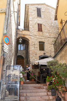 assisi,italy july 11 2020:a woman watering her plants in an alley in Assisi