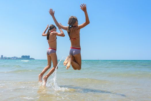 Two girls joyfully bounce on the seashore