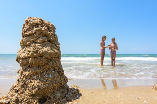 In the foreground a tower of sand, in the background two girls on the seashore