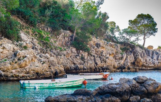 Tranquil scene with two old fishing boats moored in sea water at rocky coast