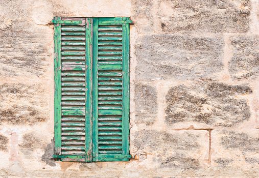 Detail view of vintage green wooden window shutters and old stone wall