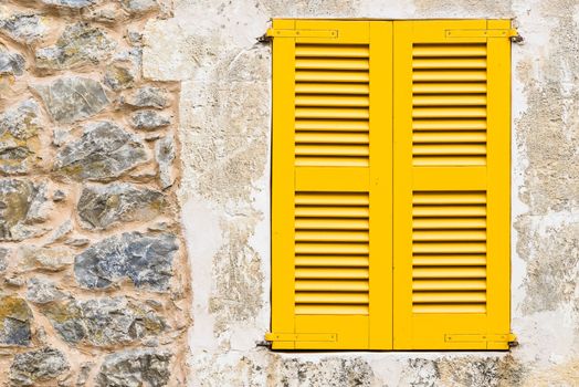 Detail view of yellow window shutters and rustic stone wall background