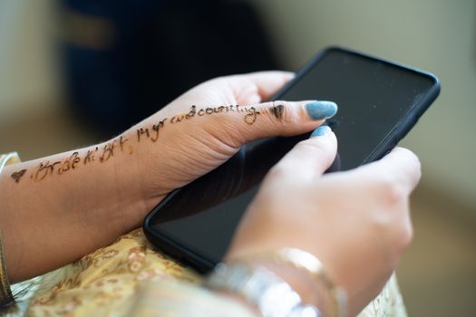 Young indian girl decked in white gold dress preparing for a wedding holding phone with words bride to be BFF written in henna tattoo. Shows the preparation for a indian wedding by the bridesmaids
