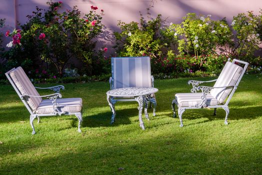 Three lawn chairs surround a wrought iron table in the garden of a South African hotel.