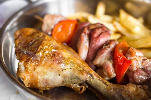 Grilled chicken drumstick, meat cooked on a spit and French fries.