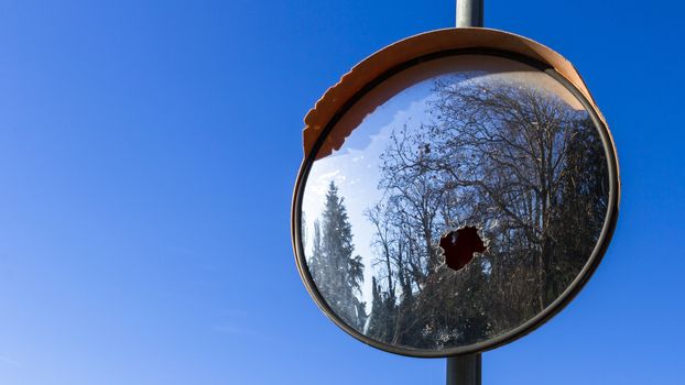 Traffic mirror, broken. Against a blue sky.