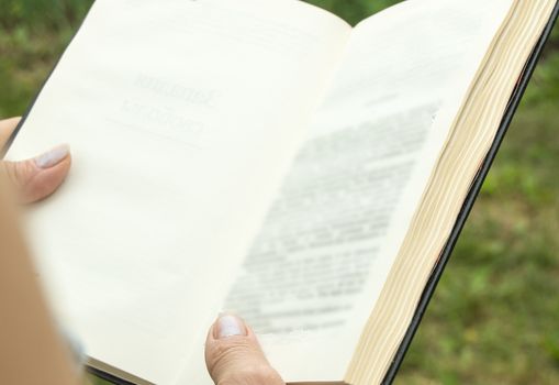 Open book in the hands of a woman, a girl reading a book, view from the back, outdoor, summer.