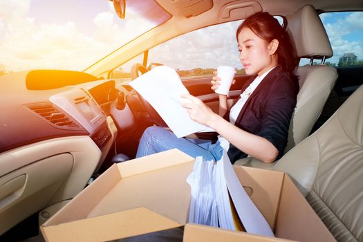 Young working woman drinking coffee and reading documents in the car before going to work