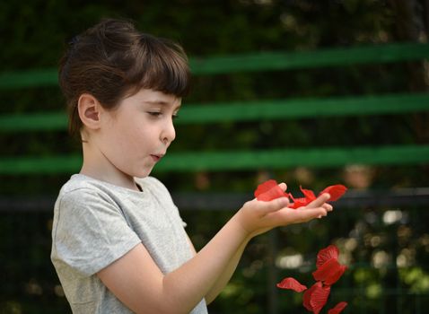 A little girl blows on red petals to make them fly from her hands, profile picture on a dark background