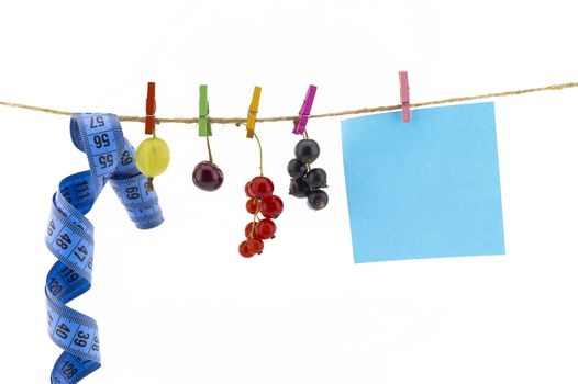 Fresh fruit, tape measure and blank sticky note hanging from clothes pegs on a rope with a gooseberry, red currants, cherry and black currants in a healthy diet concept