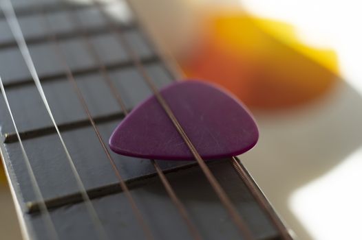 Colorful pink plectrum in guitar strings in a close up oblique angle view in a music and entertainment concept