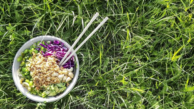 Vegan poke bowl, Hawaiian dish, with chopsticks in the grass. Cashew nuts, avocado, Red cabbage, Onion and Edamame